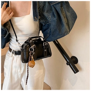 Detail view of a black glossy Boston bag with silver buckles and a basketball charm decoration
