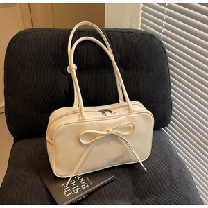 Detail of a creamy white Boston bag with a stylish bow tie on black corduroy seating
