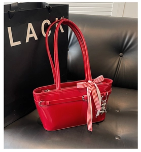 Détail du sac bandoulière en cuir verni rouge avec nœud et pendentif d'ours