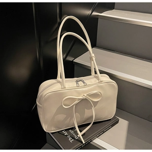Detail view of cream Boston bag with large bow and slim handles on art book