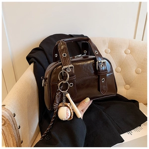 Detail of glossy brown Boston bag featuring silver eyelets and a baseball charm