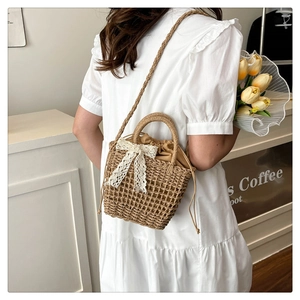Detail of hand-woven straw crossbody bag featuring white lace bow and drawstring lining