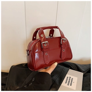 Detail view of burgundy patent leather Boston bag with metallic eyelets and silver buckles