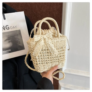 Detailed macro view of beige woven straw bucket bag featuring a delicate lace bow and drawstring