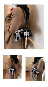 Détail du sac Boston en cuir noir brillant avec un nœud en dentelle blanche et pendentif