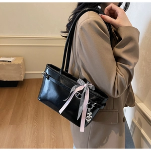 Détail du sac cabas en cuir ciré noir avec un nœud en ruban et un pendentif en forme de cœur