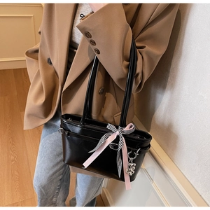 Détail du sac à bandoulière noir brillant avec nœud rose et pendentif cœur argenté