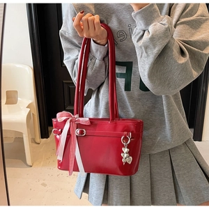 Détail du sac à main rouge en cuir verni brillant avec ruban décoratif et pendentif