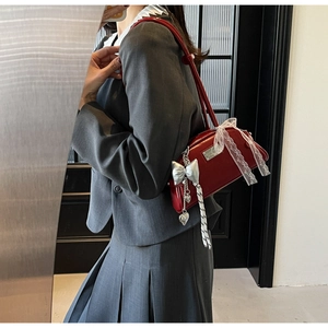 Détail du sac Boston rouge avec charm de nœud argenté et accents de rubans lacés