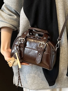 Brown glossy Boston bag with vintage motorcycle style and sporty charm on grey sweatshirt