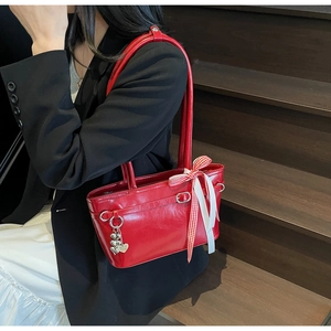 Détail du sac rouge brillant avec nœud à carreaux et pendentif en forme de cœur