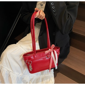 Détail du sac rouge sous le bras avec pendentif coeur et nœud à carreaux sur le cuir