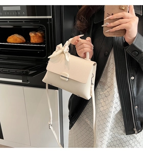 Detail of cream textured leather handbag with metal buckle and floral silk scarf accessory