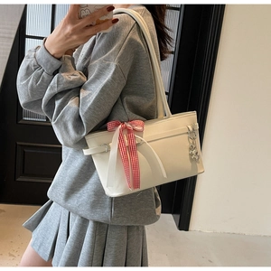 Sac sous l'aisselle crème avec nœud rouge et chaîne cœur porté par un mannequin