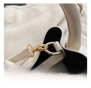 Detailed close-up of golden hardware lobster clasp on white lychee leather bucket bag