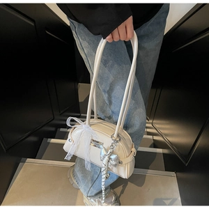 Détail du sac Boston blanc cassé avec nœud en dentelle et pendentif papillon argenté