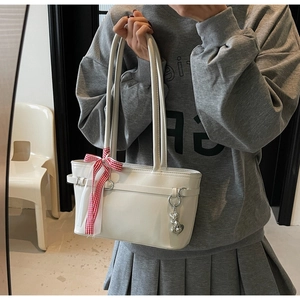 Détail du sac sous le bras blanc crème avec nœud à carreaux et pendentif cœur