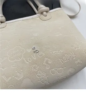 Detail shot of beige embossed bucket bag featuring silver metal logo and texture