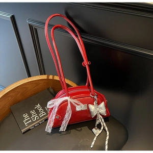 Détail du sac Boston en cuir verni rouge avec nœud en dentelle et breloque cœur