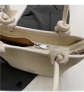 Close-up of cream embossed bucket bag featuring silver zipper and knotted rope handle detail