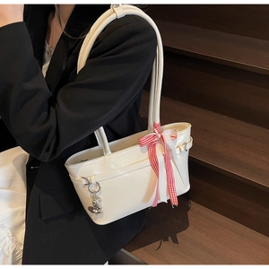 Détail d'un sac cabas crème chic avec nœud à carreaux et breloque ours argenté sur modèle