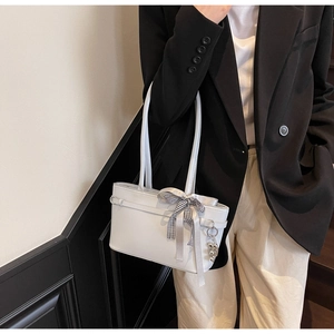 Sac hobo gris clair avec nœud à carreaux et breloque porté à l'épaule par un mannequin