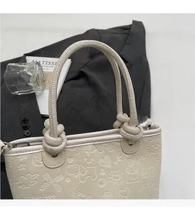 Detail of cream bucket bag with embossed cartoon patterns and knotted top handle