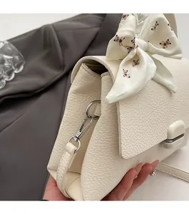 Detailed close-up of cream pebble leather bag featuring silver hardware and a silk bear scarf