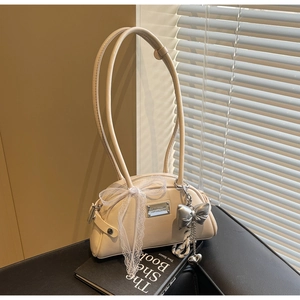 Détail du sac Boston crème avec nœud en dentelle blanche et pendentif papillon