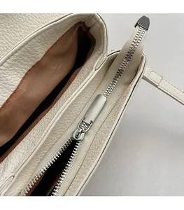 Detailed macro view of smooth silver zipper and lychee grain leather on cream handbag