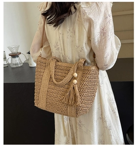 Detail of hand-woven straw basket bag featuring brown leather strap and tassel accents