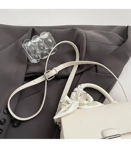 Detailed view of white pebble grain handbag with floral silk scarf and adjustable strap