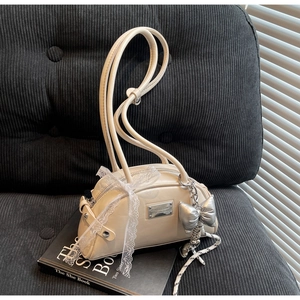 Détail d'un sac à bandoulière en cuir PU blanc cassé avec nœud en dentelle et breloque argent