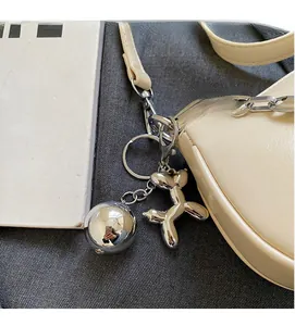 Détail du sac bandoulière en cuir beige avec chaîne argentée et charm chien