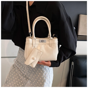 Sac à main chic en cuir crème avec breloque et fermoir argenté porté par un mannequin