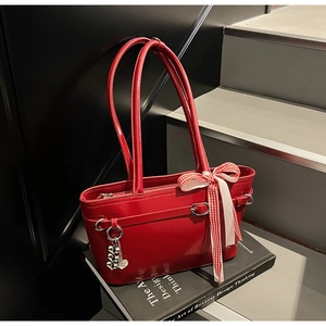 Détail du sac cabas en cuir verni rouge avec ruban à carreaux et pendentif coeur