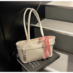 Détail du sac à bandoulière en cuir blanc avec nœud à carreaux et pendentif cœur