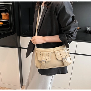 Detail of a beige faux leather crossbody bag with silver rivets and buckle pockets