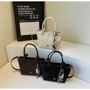 Close-up of textured embossed leather bucket bags in three colors with puppy pendant