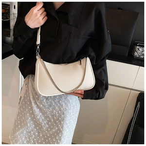 Close-up of beige crescent bag with woven texture, silver chain and adjustable strap