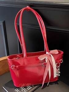 Sac à bandoulière rouge en cuir verni avec nœud et pendentif cœur sur fond noir
