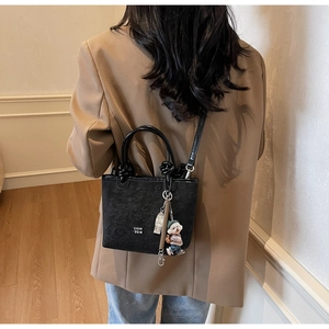 Detail view of black embossed bucket bag with COIN '2DN text and cute bear charm pendant