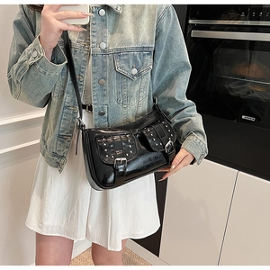 Detail of black patent leather crossbody bag with metal buckles and silver rivets