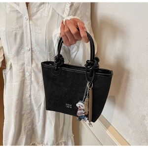 Detail of black embossed bucket bag with knot handles and cute puppy charm accessory
