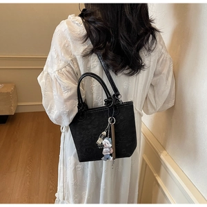 Detail of black embossed PU leather bucket bag with cute puppy pendant and gold metal logo