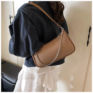 Detailed view of brown woven underarm bag with silver chain strap on model shoulder