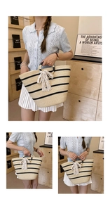 Detail of hand-woven straw tote bag with black stripes and elegant white lace bow