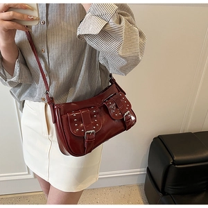 Detail of burgundy patent leather shoulder bag with silver rivets and buckle pockets