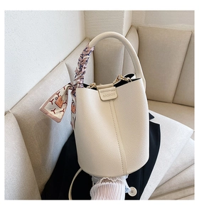 Detail of cream bucket bag in lychee leather featuring logo and floral silk scarf handle