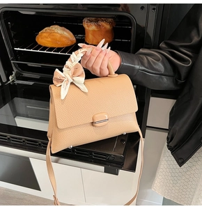 Close-up of beige leather bag with scarf-wrapped handle and metal feet on base